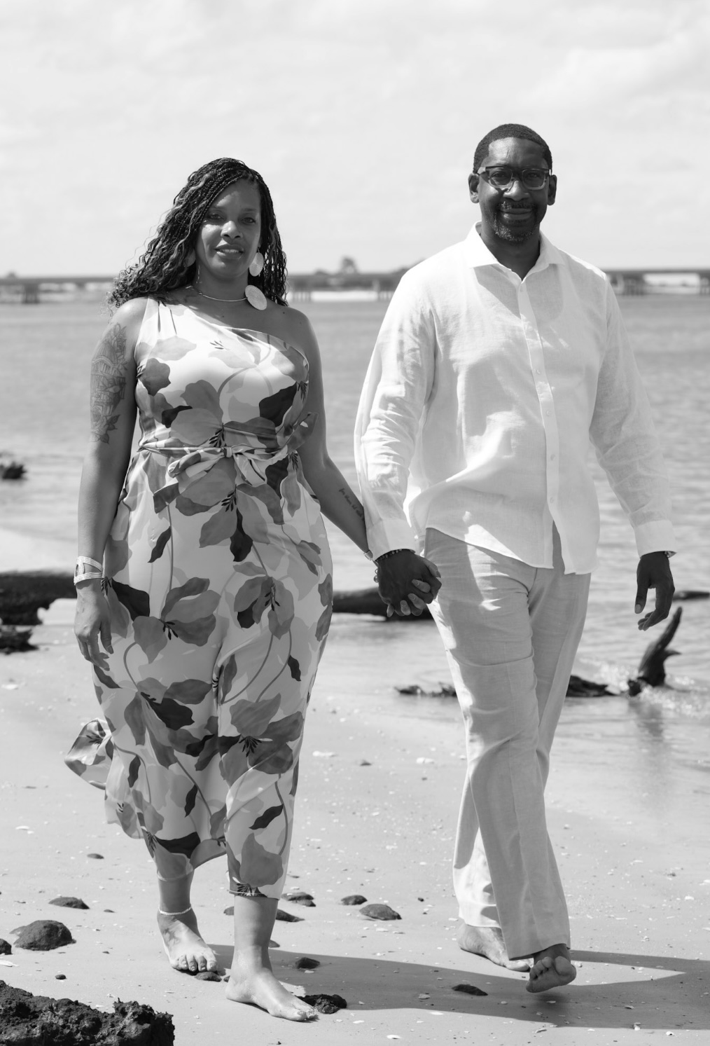 The couple walking barefoot along the shoreline, hand in hand.